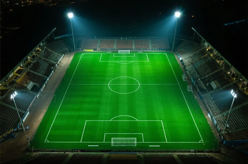 An aerial view of a pristine green soccer field with sharp white line markings under bright stadium lights